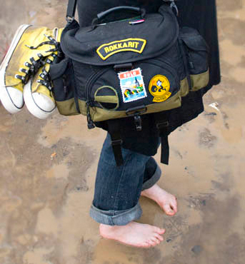 A festival photographer a woman standing in mud without shoes at a music festival